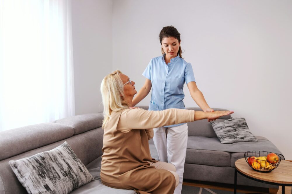 A woman helps another older woman with a stretch whilst holding her wrist