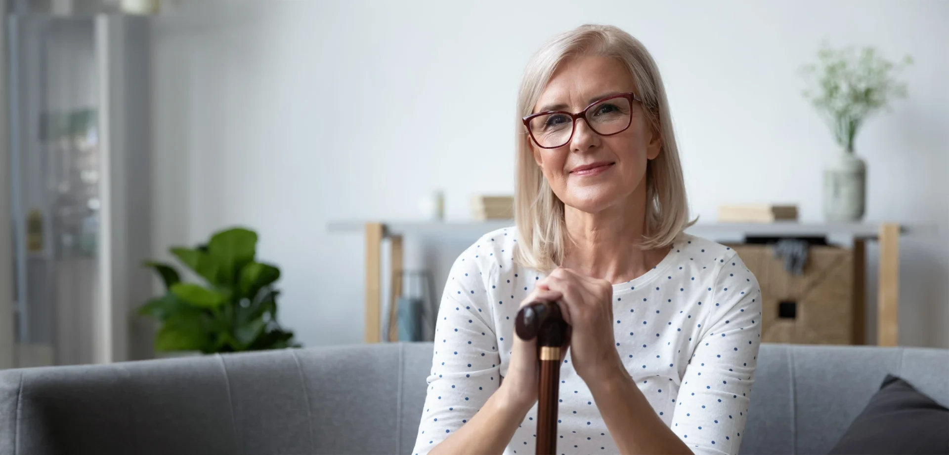 A woman looks at the camera with a smile on her face with her hands resting centrally on her walking stick